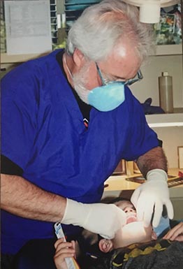 A dentist performing dental work on a patient while wearing protective gloves and a surgical mask.