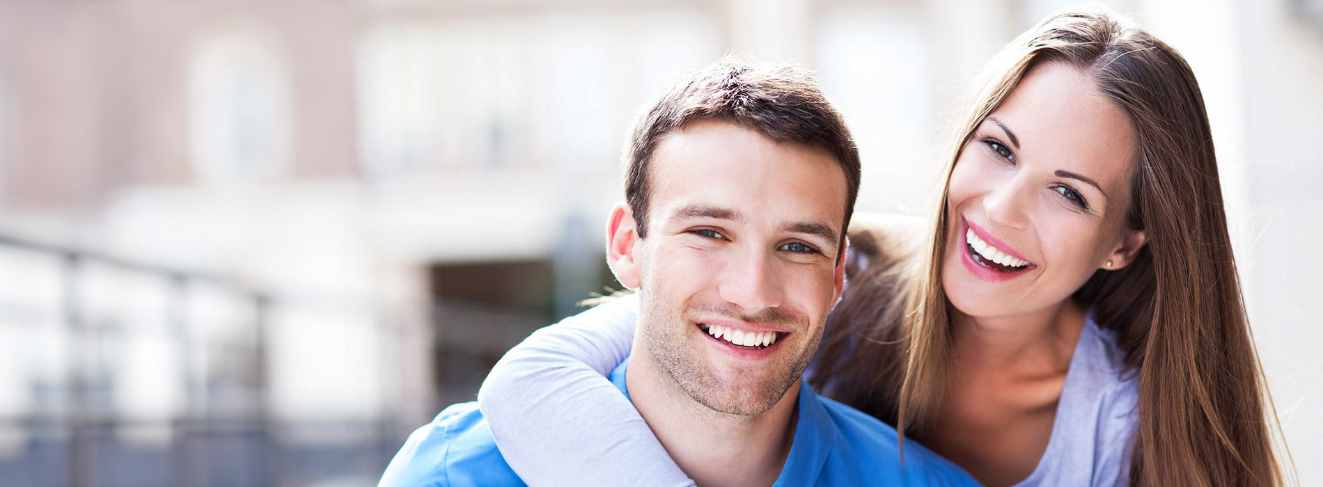 The image shows a smiling couple embracing each other against an urban backdrop.