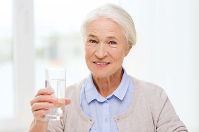 A woman holding a glass of water with her right hand, smiling slightly, and wearing a light blue cardigan.