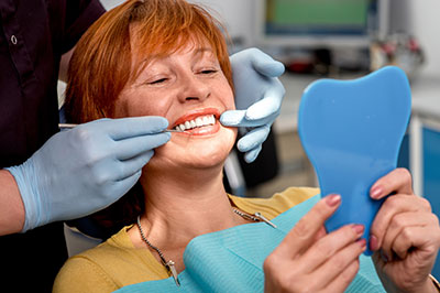 Woman receiving dental treatment with a smile on her face, holding a blue mouthguard and wearing a surgical mask.