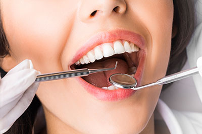 A woman receiving dental care with a focus on her open mouth revealing dental tools inside.