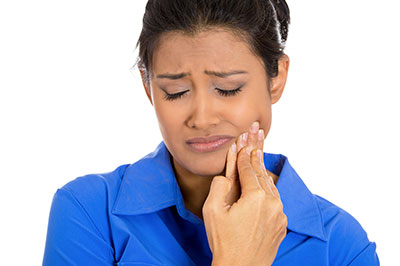 A woman with dark hair wearing a blue shirt, looking down at her hand with a concerned expression while holding an object that appears to be a toothbrush.