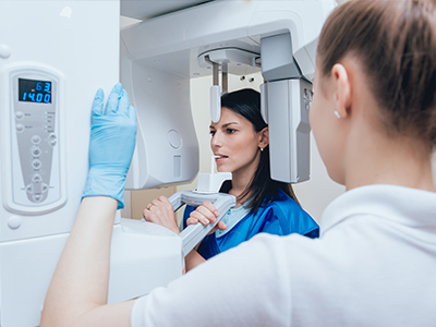 A woman in blue scrubs is operating a large white 3D scanner while another person looks on, both are in a medical setting.