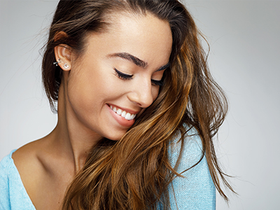 The image shows a young woman with long hair smiling at the camera, with her head slightly tilted.