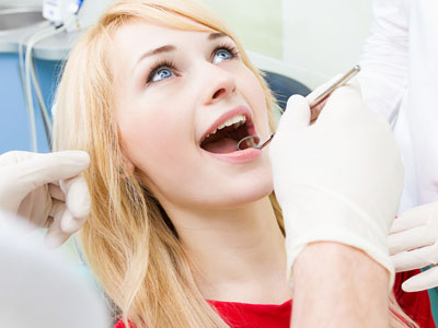 A woman receiving dental care, with a dentist performing a procedure while she smiles and looks up.