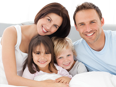 A family of four posing together on a bed with a man and woman smiling at the camera.