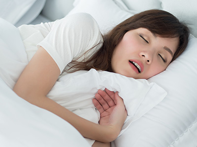 Woman asleep on bed with eyes closed and mouth open.