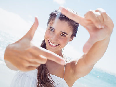 A woman taking a selfie with her hand held up against a bright sky background.